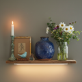 Shelf vignette mixing a hand-thrown ceramic vessel, vintage brass candlestick, wildflowers in a glass jar, and a flea market find — high-low design in practice